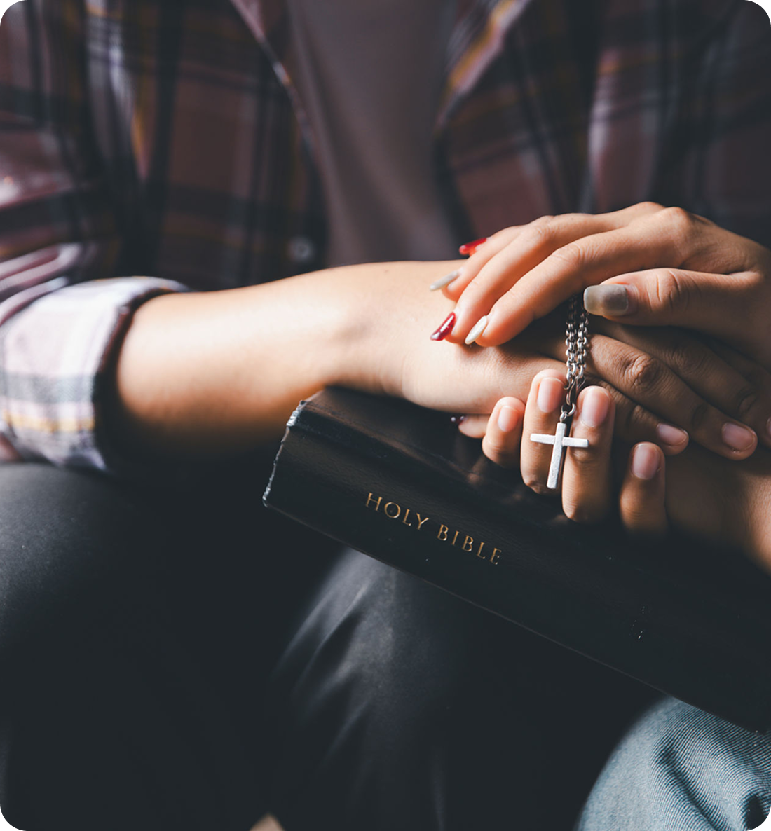 Hands holding Bible and cross necklace.