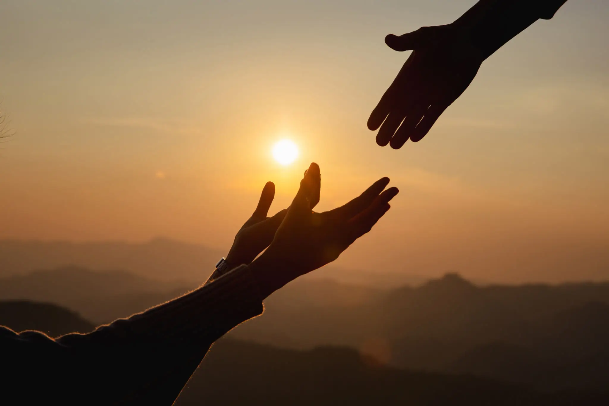 Hands reaching towards each other at sunset.